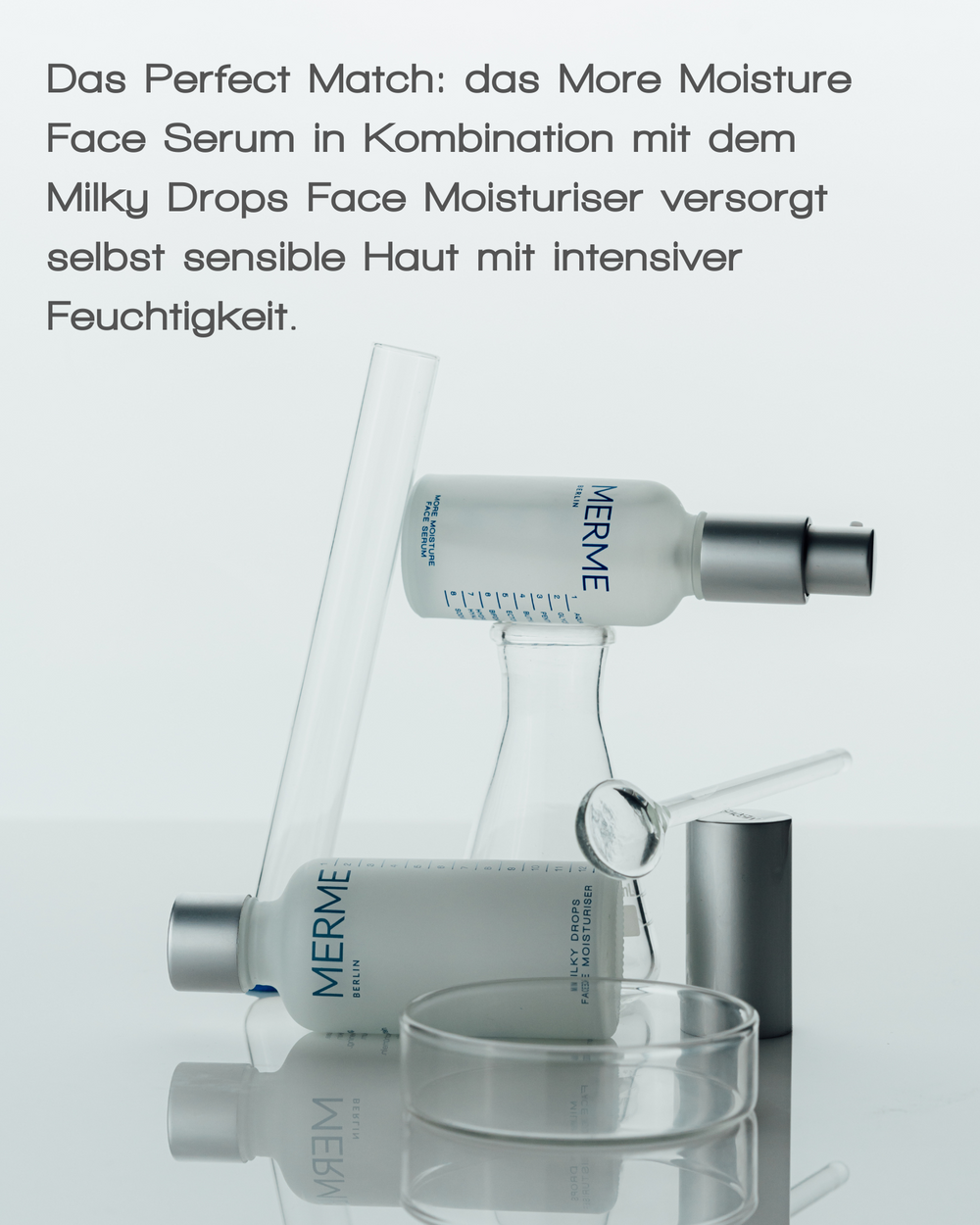 Drei Flaschen des MERME Berlin MORE MOISTURE FACE SERUM sind kunstvoll in Laborgläsern gestapelt. Der deutsche Text hebt Hyaluronsäure hervor und empfiehlt die Kombination des Serums mit der Milky Drops Gesichtsfeuchtigkeitscreme für intensive Feuchtigkeitsversorgung, die auch für empfindliche Haut geeignet ist.
