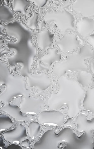 Nahaufnahme von Wassertropfen, die auf einer glatten, silbermetallischen Oberfläche verstreut sind und ein abstraktes Muster mit unterschiedlichen Größen und organischen Formen erzeugen.