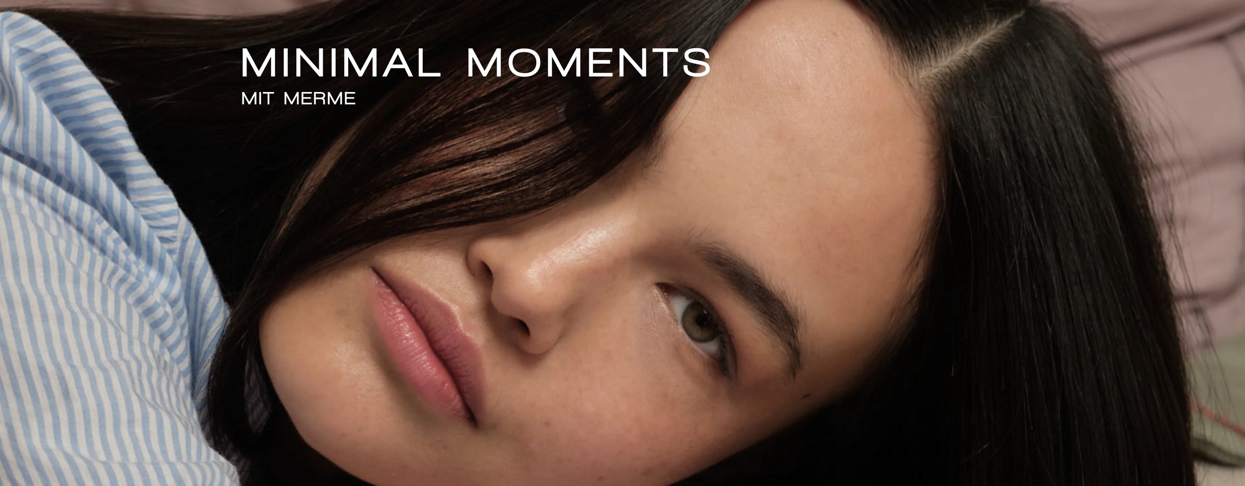 Nahaufnahme einer jungen Frau mit langen dunklen Haaren, die auf der Seite liegt und ruhig in die Kamera blickt. Oben links im Bild erscheint der Text „MINIMAL MOMENTS MIT MERME“.