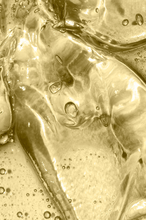 Nahaufnahme von klaren Eiswürfeln mit Blasen darin, die mit einem goldgelben Farbton getönt sind, wodurch eine glänzende und abstrakte Textur entsteht.