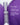 Eine violett-weiße Flasche MERME Berlin PRIME. REFINE. SEAL. Gesichtsserum steht zwischen zwei großen violetten Formen, mit deutschem Text, der Vorteile wie DNA-Reparatur, verkleinerte Poren und weniger Fältchen hervorhebt.