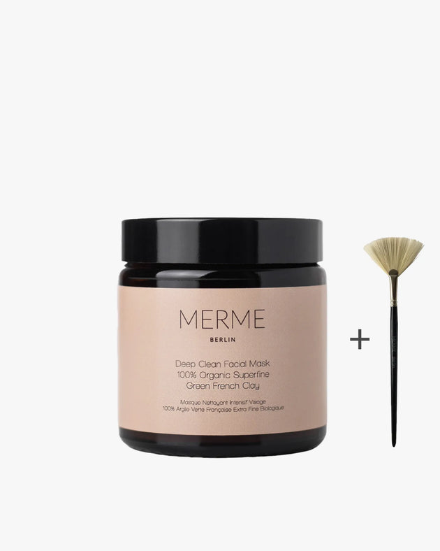 Ein Tiegel MERME Berlin DEEP CLEAN FACIAL MASK mit beigem Etikett steht neben einem kleinen Fächerpinsel mit schwarzem Griff und hebt natürliche Mineralien auf einem schlichten weißen Hintergrund hervor.