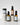 Vier bernsteinfarbene und schwarze Flaschen und Tiegel von MERME Berlin, darunter das BAKUCHIOL 3% FACIAL SERUM – Natural Retinol Alternative Packs, stehen auf weißen Marmorsockeln. Hellblaue und beige Etiketten sorgen für einen minimalistischen Look auf schlichtem weißem Hintergrund.