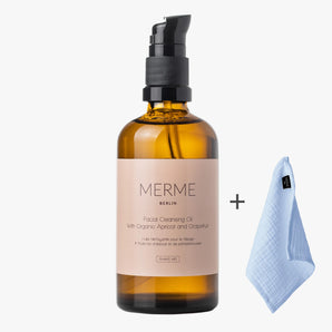 Bernsteinfarbene Flasche MERME Berlin FACIAL CLEANSING OIL mit Grapefruit und schwarzem Pumpspender, präsentiert neben einem gefalteten hellblauen Reinigungstuch auf schlichtem weißem Hintergrund.