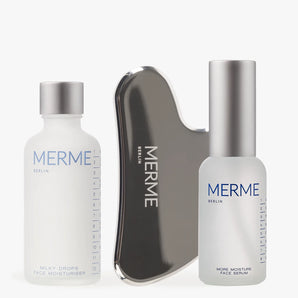 Das MOISTURISE & MASSAGE SET von MERME Berlin enthält eine Milky Drops Face Moisturiser, ein Gua Sha-Tool und ein More Moisture Face Serum mit Hyaluronsäure, alles elegant angeordnet auf weißem Hintergrund.