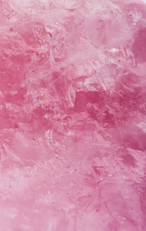Nahaufnahme einer rauen, rosa Kristalloberfläche mit unterschiedlichen Texturen und durchscheinenden Bereichen, die natürliche Muster und Risse zeigen.