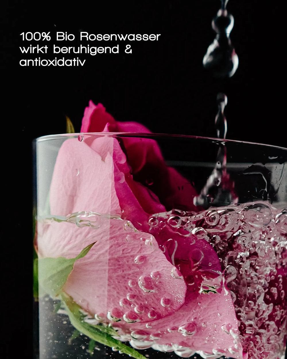 Eine rosa Rose und Blasen füllen ein Glas ANTIOXIDANT MIST WITH ROSE QUARTZ von MERME Berlin, während Wasser hineintropft. Deutscher Text: „100 % Bio-Rosenwasser wirkt beruhigend & antioxidativ“ – ideal als Gesichtsspray oder für die sanfte Rosenquarz-Pflege.