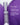 Eine violett-silberne Flasche des TEXTURE & HYDRATION DUO von MERME Berlin ist zwischen zwei glänzenden violetten Formen platziert, mit weißem deutschem Text, der Niacinamid, Bakuchiol und NAD+ für fortschrittliche Hautpflegevorteile auflistet.