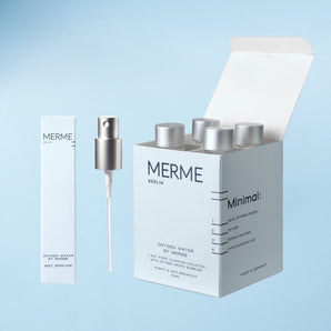 Eine weiße "MERME Berlin"-Schachtel hält Flaschen mit silbernen Verschlüssen. Daneben suggerieren die schlanke Dose OXYGEN WATER BY MERME 4-WOCHEN-SET und eine silberne Sprühdüse fortschrittliche Sauerstoff-Microbubble-Technologie auf hellblauem Hintergrund.