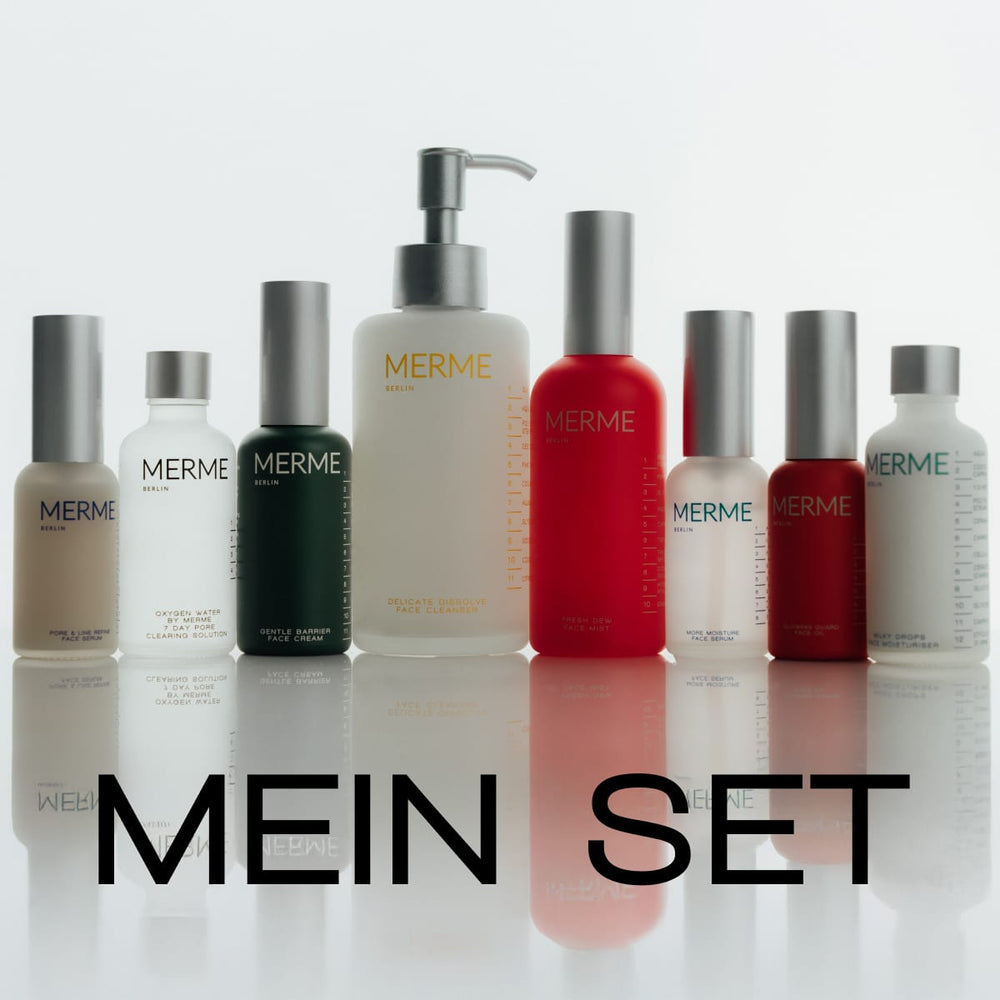 Neun MERME Berlin-Pflegeflaschen und -tiegel in verschiedenen Größen und Farben sind auf einer spiegelnden Fläche abgebildet, am unteren Bildrand steht in großen schwarzen Buchstaben "Mein Set".