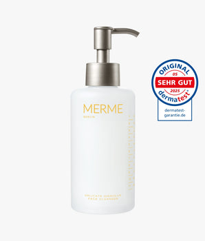 Eine weiße Pumpflasche mit der Aufschrift "MERME Berlin Delicate Dissolve Face Cleanser" steht neben einem runden blau-roten Dermatest-Siegel mit der Aufschrift "Sehr Gut 2025" und "Original dermatest-garantie.de" auf weißem Hintergrund.