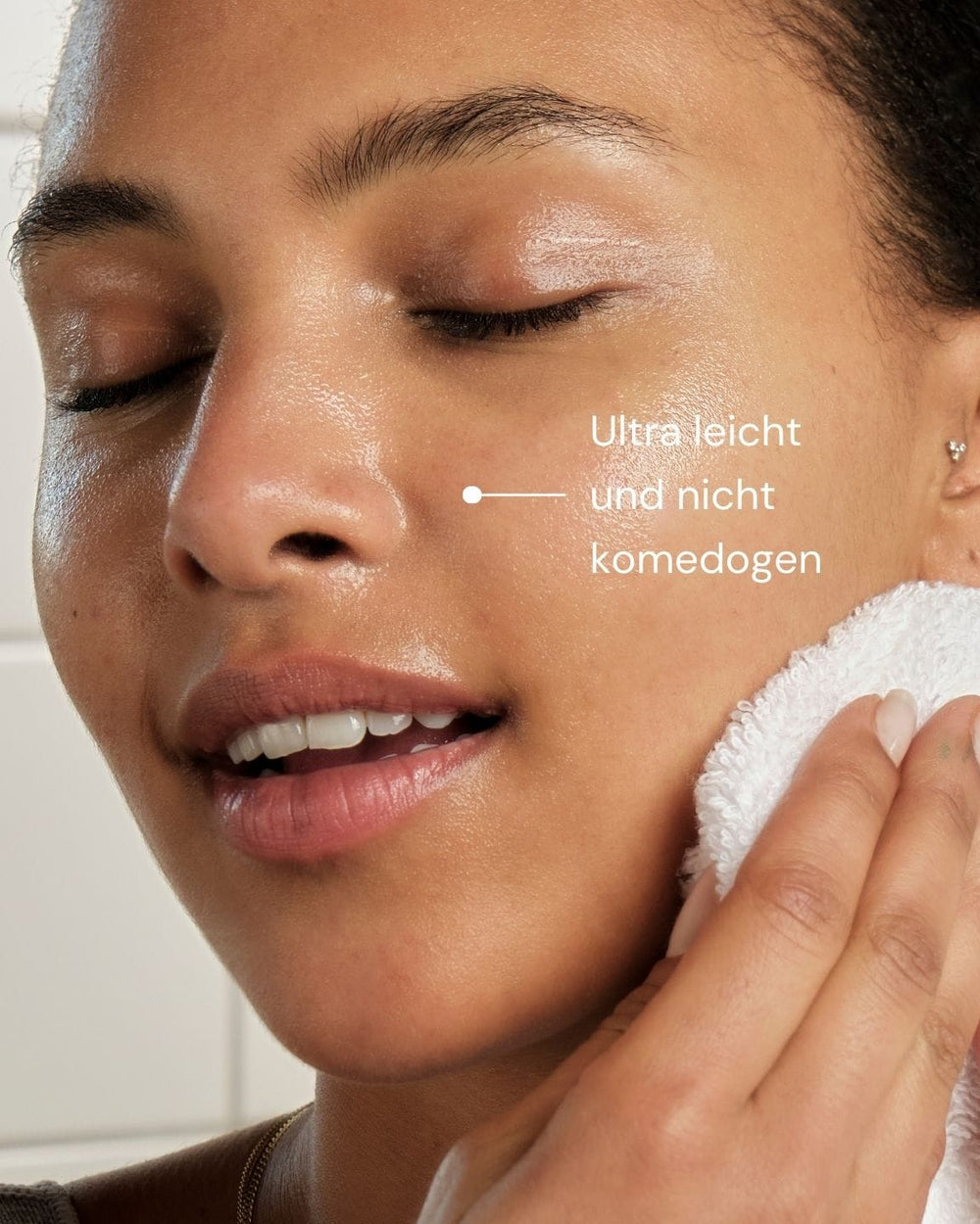 Eine Person mit strahlender Haut, die Augen geschlossen und lächelnd, drückt sanft ein Handtuch auf ihr Gesicht - ideal für empfindliche Haut. Der deutsche Text lautet "Ultra leicht und nicht komedogen" und wirbt für den Delicate Dissolve Face Cleanser von MERME Berlin.