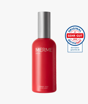 Ein roter MERME Berlin Fresh Dew Face Mist Flakon mit silberner Kappe, ideal als Gesichtsspray für zusätzlichen Glow, steht neben einem runden blau-weißen Dermatest "SEHR GUT" Qualitätssiegel für 2026.