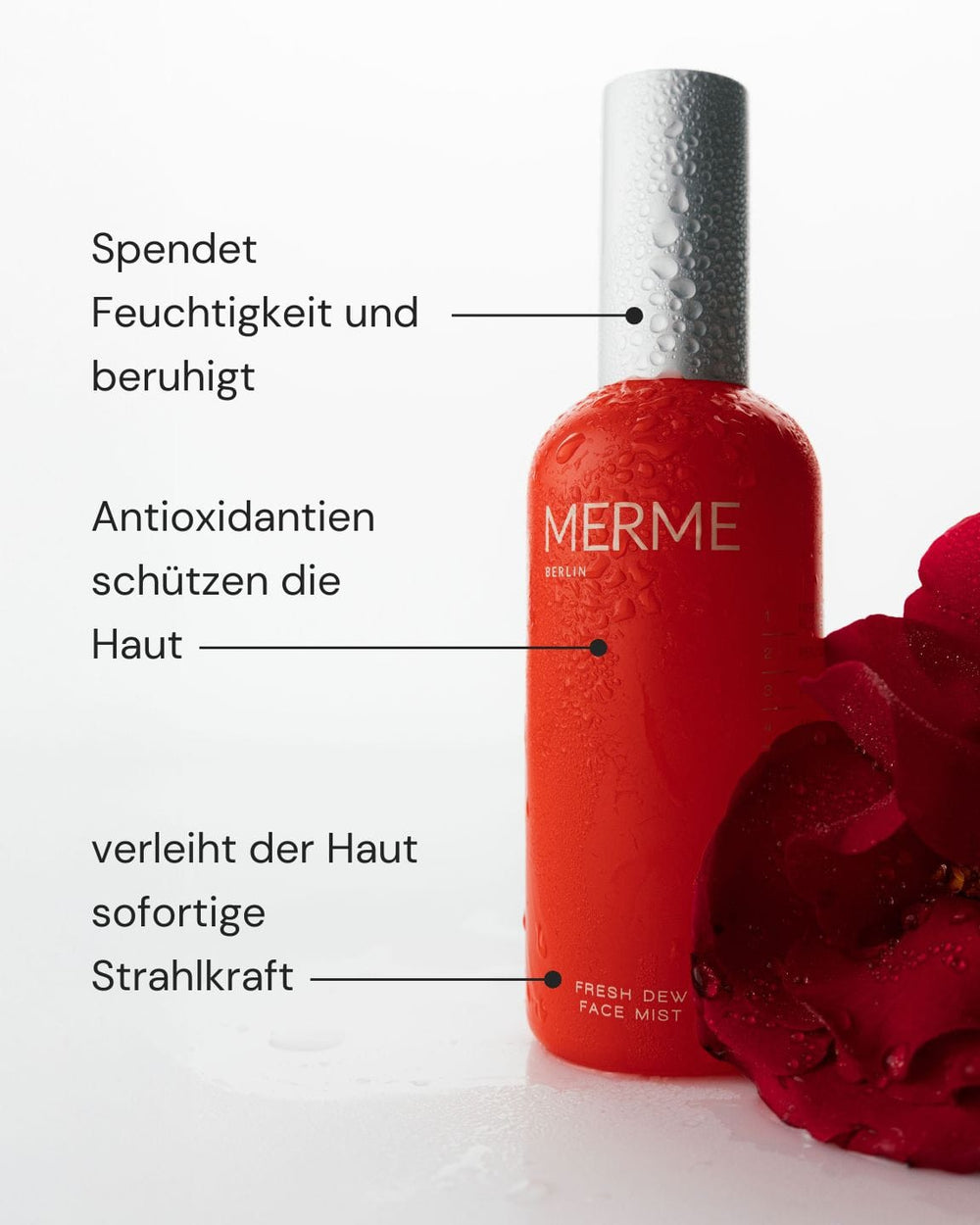Eine rote MERME Berlin Fresh Dew Face Mist Flasche mit Wassertropfen steht aufrecht neben einer roten Rose auf einer weißen Fläche. Der deutsche Text unterstreicht die feuchtigkeitsspendende, beruhigende, antioxidative und die Haut aufhellende Wirkung.