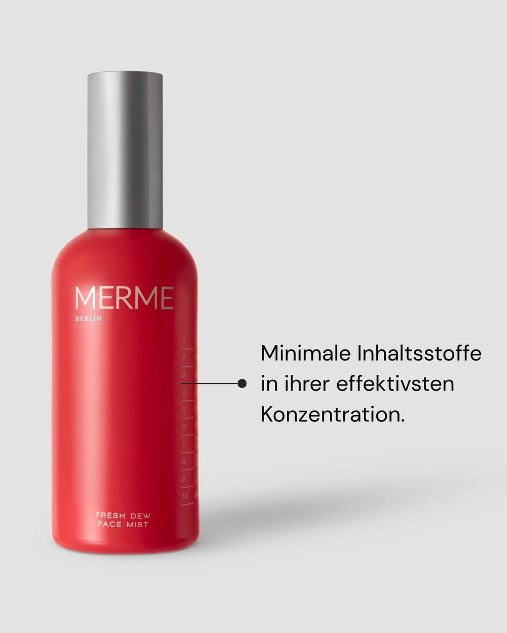 Eine rote Flasche mit der Aufschrift "MERME Berlin Fresh Dew Face Mist" und einer silbernen Kappe steht auf einem grauen Hintergrund. Darauf zeigt eine Linie mit deutschem Text über minimale Inhaltsstoffe in effektiver Konzentration für Glow und Hautaufhellung.