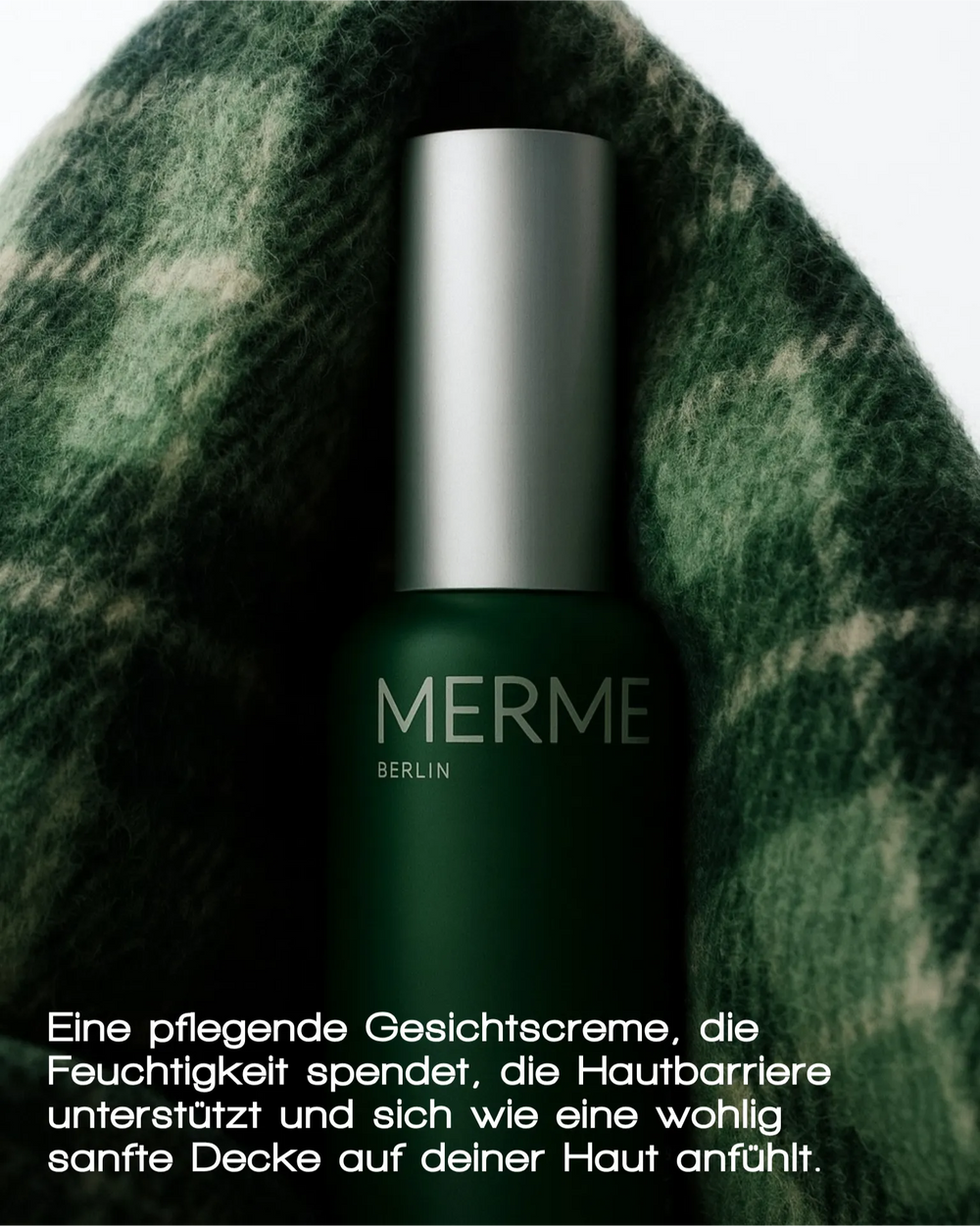 Ein dunkelgrüner Flakon der MERME Berlin GENTLE BARRIER FACE CREAM mit einer silbernen Kappe ruht auf einem weichen, grün gemusterten Stoff, während ein deutscher Text die feuchtigkeitsspendende und hautberuhigende Wirkung hervorhebt.