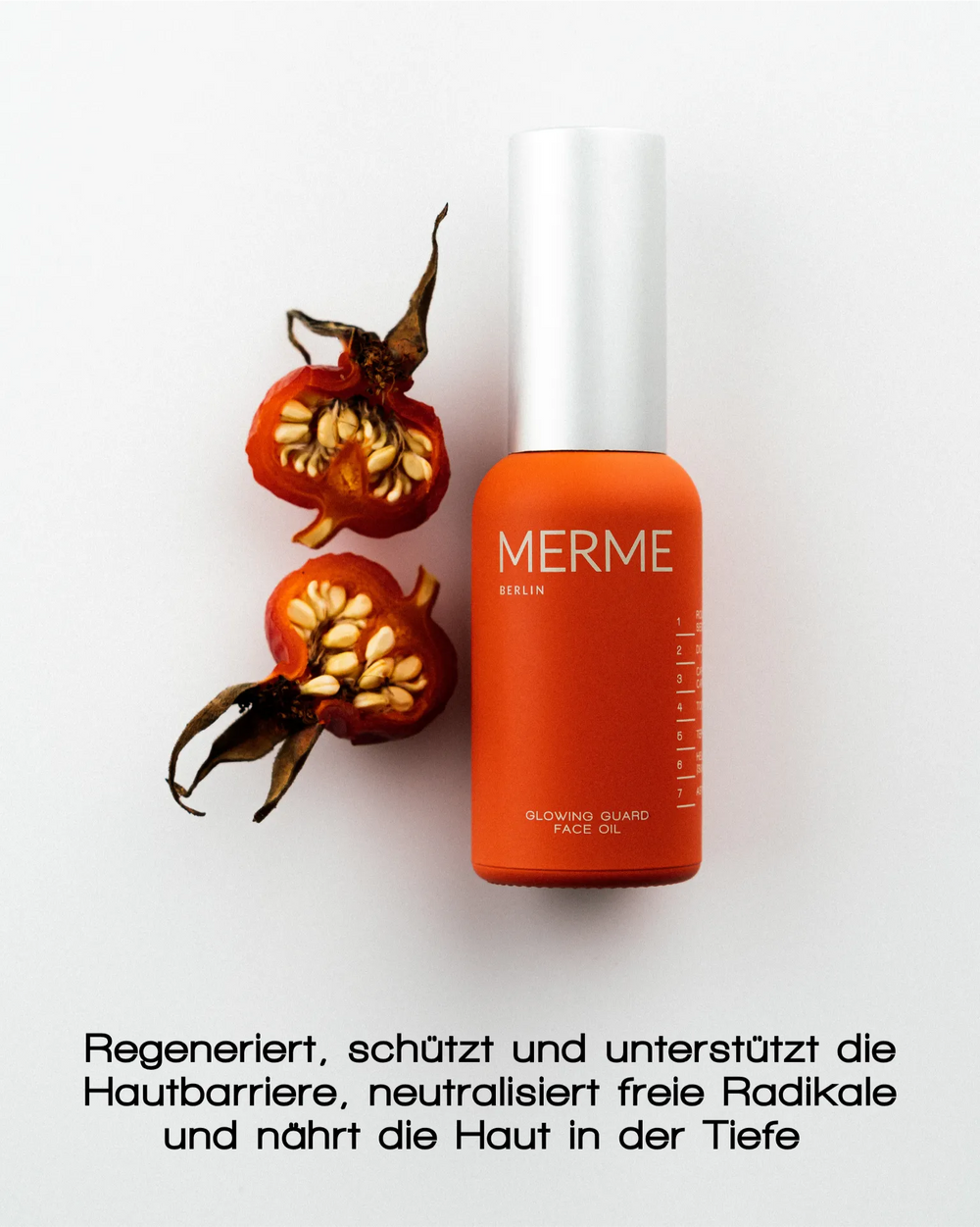 Eine orangefarbene Flasche MERME Berlin GLOWING GUARD FACE OIL steht neben einer halbierten Hagebuttenfrucht auf einem weißen Hintergrund. Der deutsche Text darunter hebt die Vorteile für die Regeneration der Haut und einen natürlich strahlenden Teint hervor.