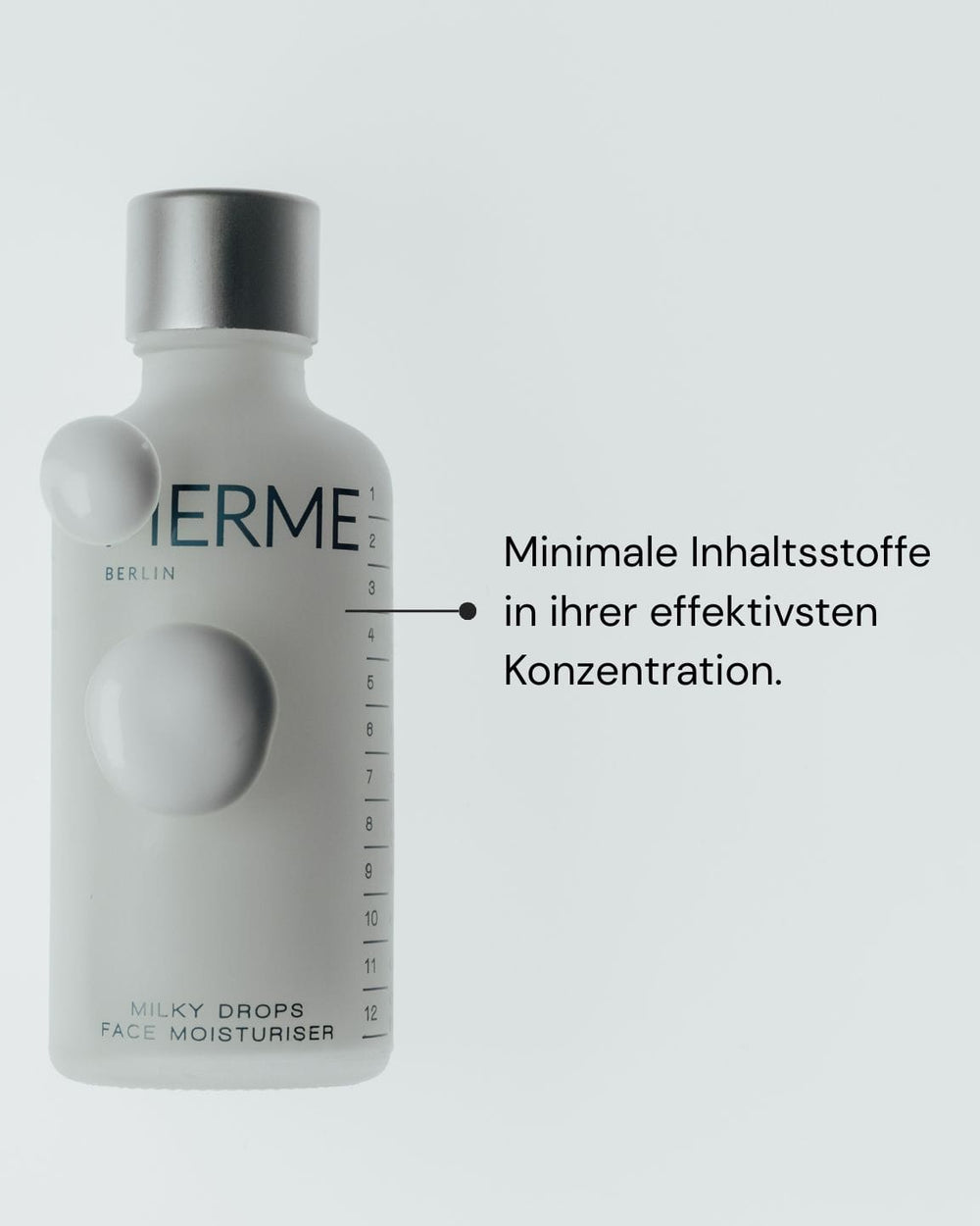 Eine weiße Flasche mit der Aufschrift "MERME Berlin Milky Drops Face Moisturiser" ist mit einer seitlichen grafischen Skala versehen. Der deutsche Text lautet: "Minimale Inhaltsstoffe in ihrer effektivsten Konzentration." Mit Ceramid für intensive Feuchtigkeitszufuhr.