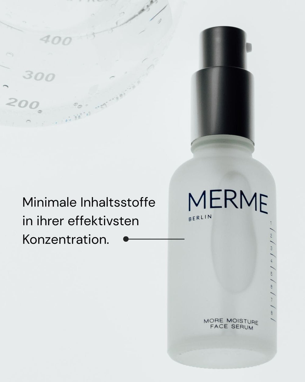 Eine Milchglasflasche des More Moisture Face Serum von MERME Berlin mit schwarzer Pumpe steht neben einem deutschen Text: "Minimale Inhaltsstoffe in ihrer effektivsten Konzentration". Oben links ist eine klare Flüssigkeit mit Messmarken zu sehen.