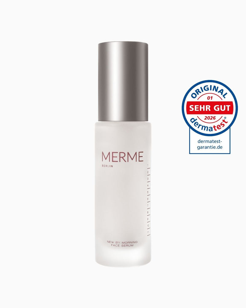 Ein Milchglasflakon von MERME Berlin New by Morning Retinal Face Serum mit einem metallischen Verschluss steht neben einer runden blau-roten Dermatest-Zertifizierungsplakette "SEHR GUT 2026".
