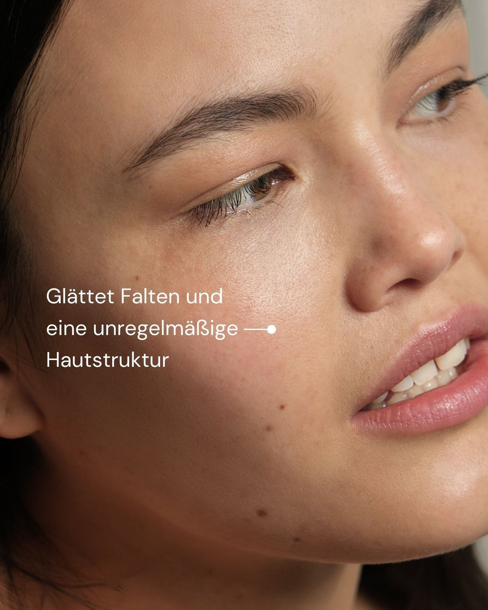 Eine Nahaufnahme der glatten, klaren Haut einer Frau mit deutschem Text: "Glättet Falten und eine unregelmäßige Hautstruktur", um das New by Morning Retinal Face Serum von MERME Berlin vorzustellen, das Falten und eine unregelmäßige Hautstruktur glättet.