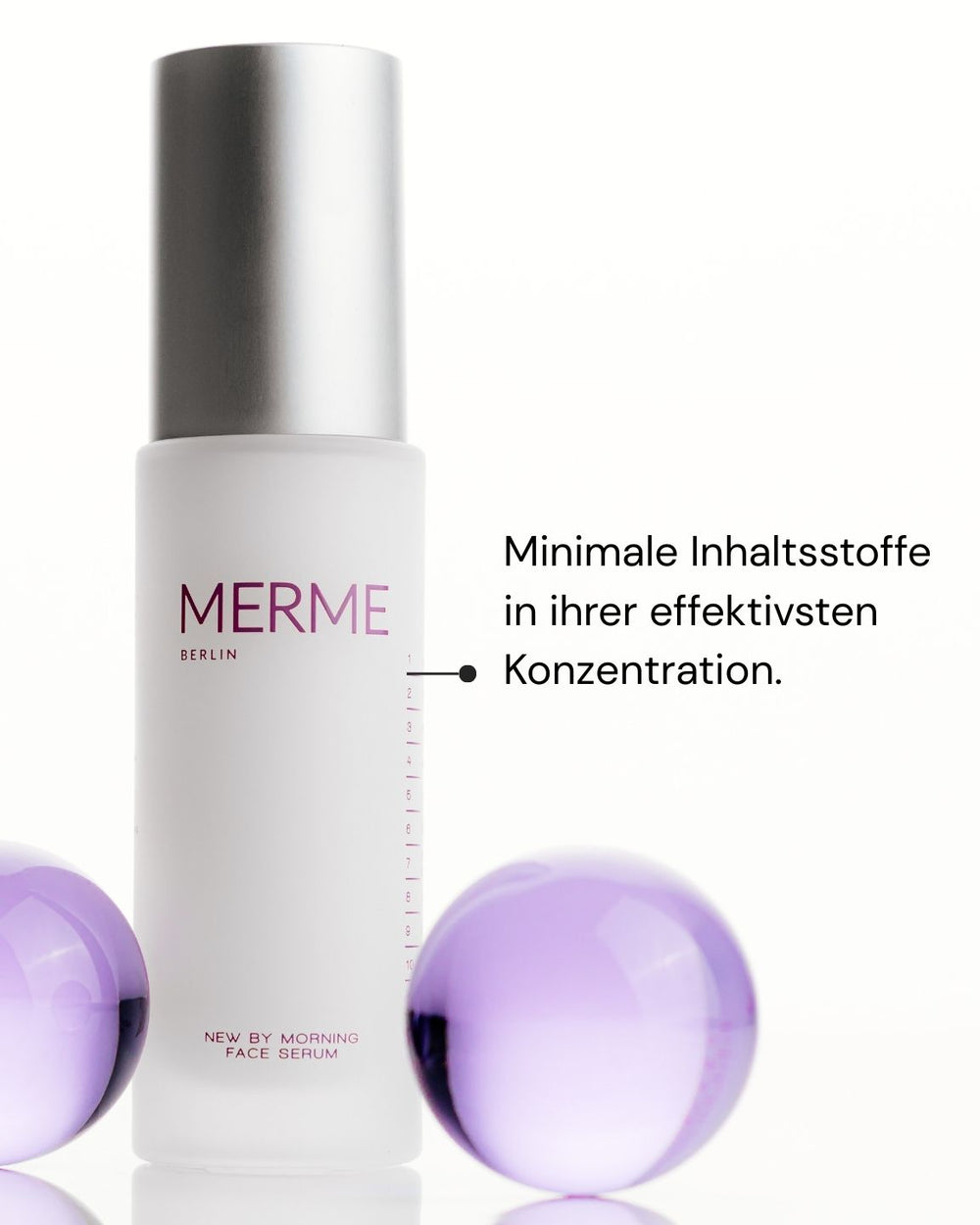 Ein weißer Flakon von MERME Berlin New by Morning Retinal Face Serum mit einer silbernen Kappe steht zwischen zwei lila Kugeln. Der deutsche Text lautet: "Minimale Inhaltsstoffe in ihrer effektivsten Konzentration.