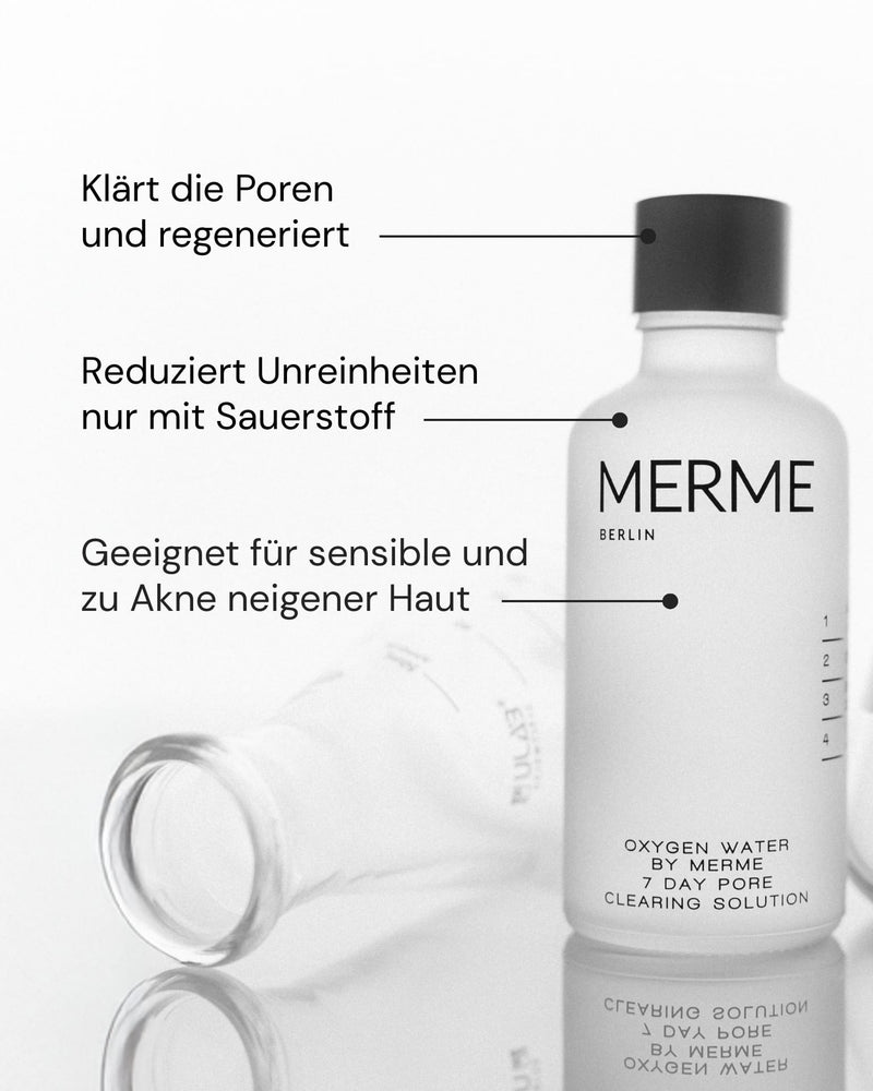 Eine durchsichtige Flasche mit der Aufschrift "MERME Berlin OXYGEN WATER PORE CLEARING SOLUTION - 4 WOCHEN" steht aufrecht neben einer anderen; der deutsche Text hebt die Porenreinigung mit der Oxygen Microbubble Technology, die Reduzierung von Hautunreinheiten und die Eignung für empfindliche Haut hervor.