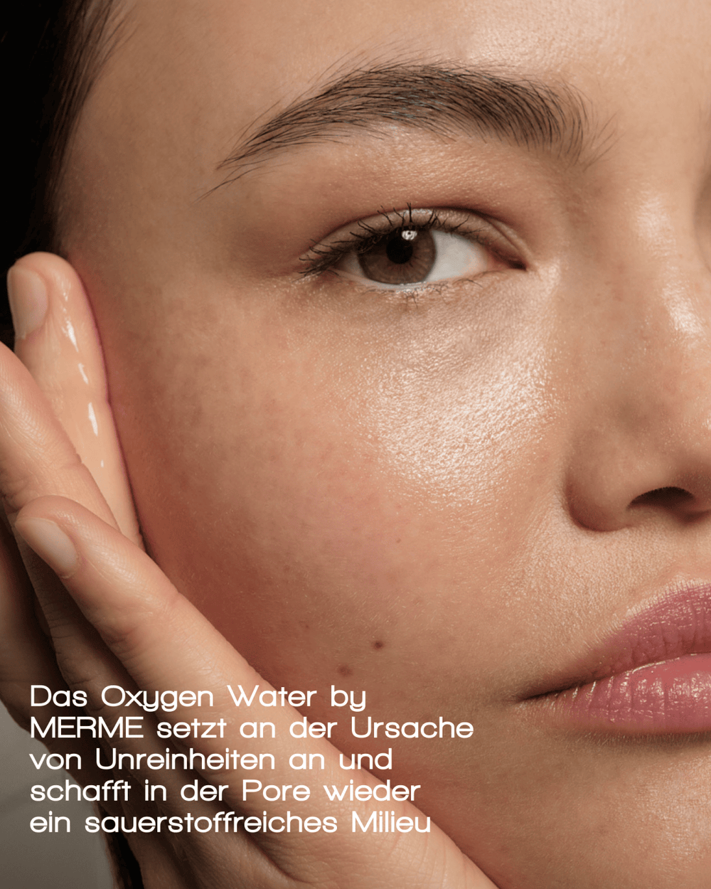 Nahaufnahme des Gesichts einer Frau mit klarer Haut, die ihre Wange berührt. Der deutsche Text am unteren Rand hebt OXYGEN WATER BY MERME von MERME Berlin hervor, mit Sauerstoff-Microbubble-Technologie für gesunde Poren und Sauerstoffzufuhr.