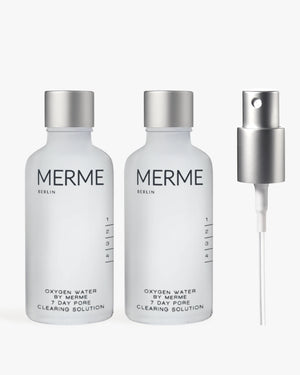Zwei durchsichtige Flaschen mit der Aufschrift "OXYGEN WATER BY MERME 2-WOCHEN-SET" von MERME Berlin stehen nebeneinander und sind mit der fortschrittlichen Sauerstoff-Microbubble-Technologie für eine effektive Porenreinigung ausgestattet. Rechts daneben sitzt eine silberne Sprühdüse auf einem schlichten Hintergrund.