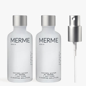 Zwei durchsichtige Flaschen mit der Aufschrift "OXYGEN WATER BY MERME 2-WOCHEN-SET" von MERME Berlin stehen nebeneinander und sind mit der fortschrittlichen Sauerstoff-Microbubble-Technologie für eine effektive Porenreinigung ausgestattet. Rechts daneben sitzt eine silberne Sprühdüse auf einem schlichten Hintergrund.