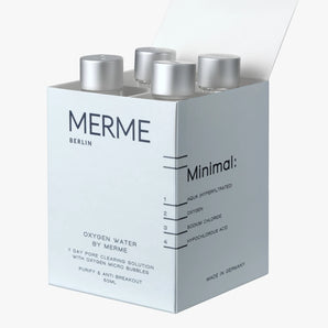 In einer teilweise geöffneten weißen Schachtel mit der Aufschrift "MERME Berlin OXYGEN WATER 4-WOCHEN-SET" befinden sich vier Flaschen. Die minimalistische Verpackung listet nur wenige Inhaltsstoffe auf und behauptet, die Haut zu reinigen und Hautausbrüche zu verhindern.