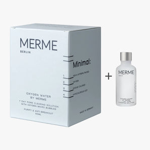 Eine weiße Schachtel mit der Aufschrift "MERME Berlin Oxygen Water Pore Clearing Solution - 4 Wochen" steht neben einer durchsichtigen Flasche mit weißem Verschluss, beide mit minimalistischem Design und schwarzem Text, der dieses 4-Wochen-Porenreinigungsspray hervorhebt.