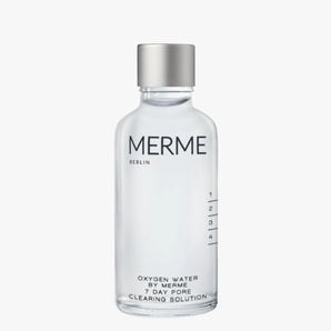 Eine Klarglasflasche mit einer silbernen Kappe und der Aufschrift "MERME Berlin" enthält eine Sauerstoffwasserprobe, eine transparente Flüssigkeit mit Messmarkierungen an der Seite. Auf dem Etikett steht "Oxygen Water Sample by MERME Berlin".