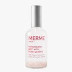 Eine durchsichtige Sprühflasche mit der Aufschrift MERME Berlin Antioxidant Mist with Rose Quartz", mit Bio-Rosenwasser und sichtbaren Rosenquarzkristallen am Boden und einer silbernen Kappe, sorgt für einen Feuchtigkeitsschub auf weißem Grund.