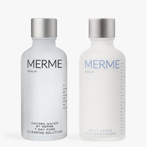 Zwei Flaschen von MERME Berlin: Links-CLEAR & SOOTHE mit einer glänzenden Silberkappe; rechts-Milky Drops Face Moisturiser mit einer matten Silberkappe.