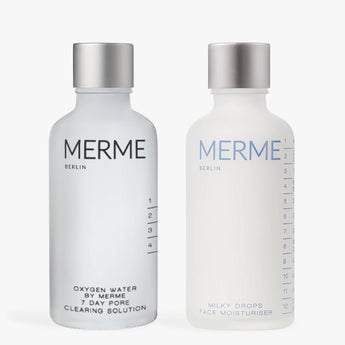 Zwei Flaschen von MERME Berlin: Links-CLEAR & SOOTHE mit einer glänzenden Silberkappe; rechts-Milky Drops Face Moisturiser mit einer matten Silberkappe.