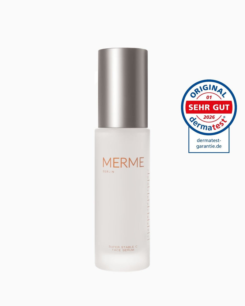 Ein Milchglasflakon von MERME Berlin Super Stable C Face Serum mit einer Metallkappe steht neben einem kreisförmigen Dermatest "Sehr Gut" Qualitätssiegel 2026.
